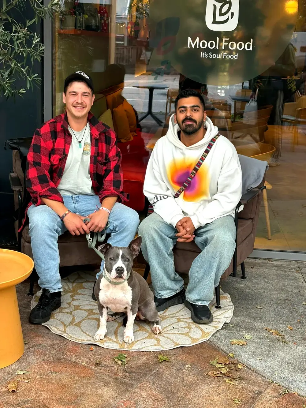 Die beiden Musiker sitzen gemeinsam vor einem Café, zwischen ihnen ein Hund