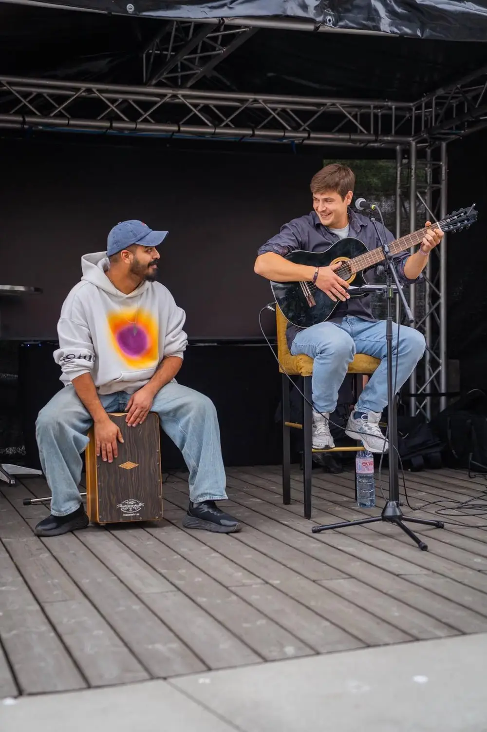 Die beiden Musiker auf einer Open-Air-Bühne, einer am Cajón, einer mit Gitarre; sie schauen sich lachend an